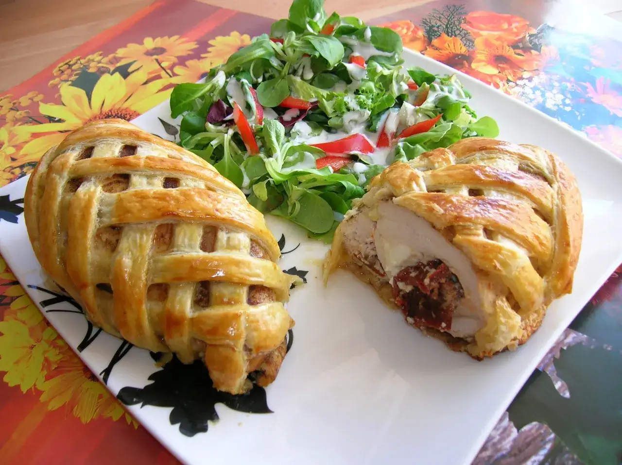 Pyszny kurczak w cieście francuskim z mozzarellą i suszonymi pomidorami, podany z sałatką.