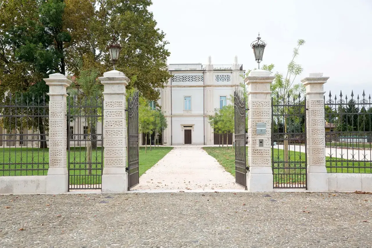 Ingresso della bottega veneta sede, con cancello aperto, viale di ghiaia e villa bianca.