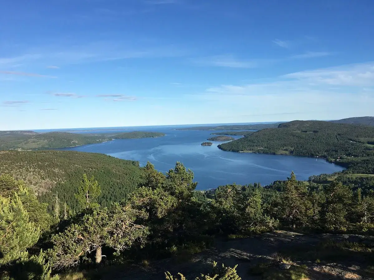 Vacker utsikt &ouml;ver en stor sj&ouml; med &ouml;ar, omgiven av skogkl&auml;dda kullar. En vy fr&aring;n h&ouml;ga kusten en solig dag.