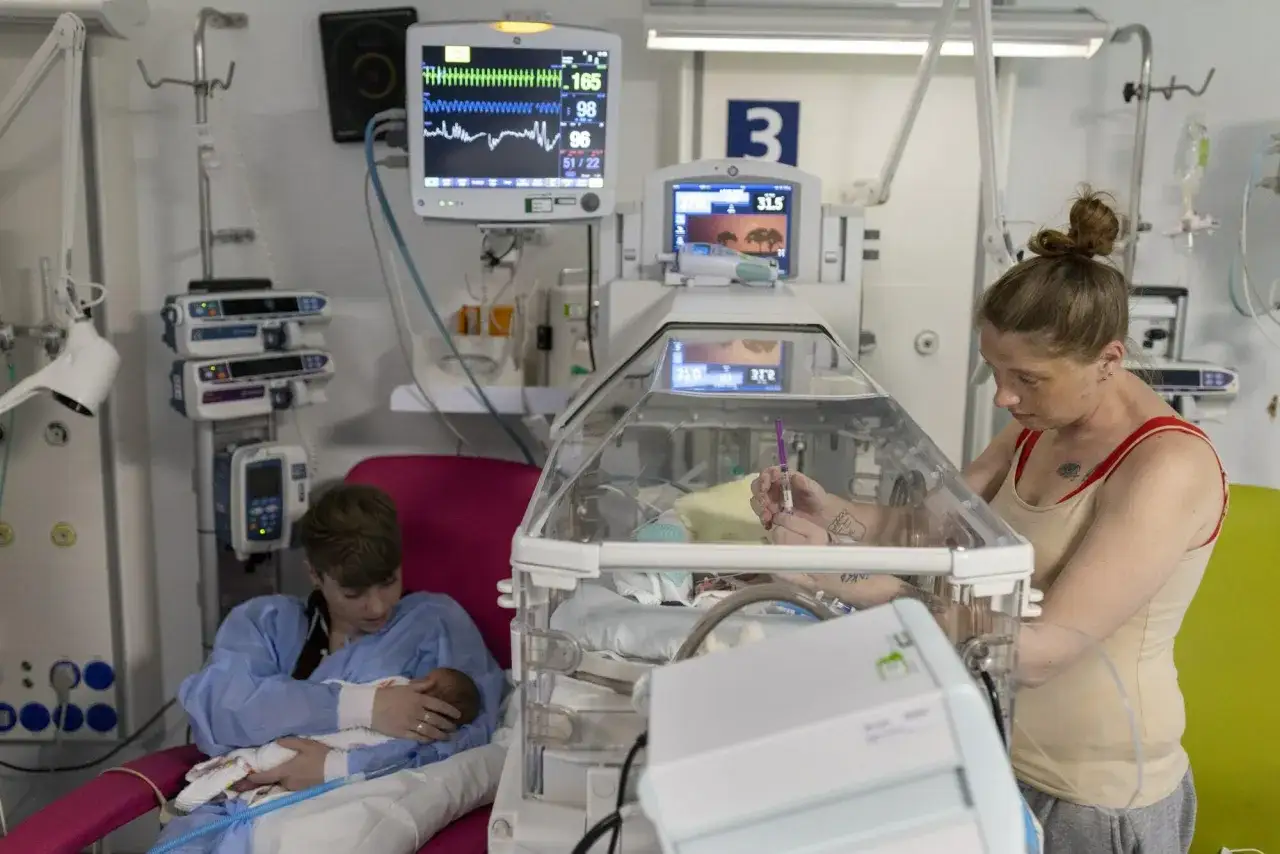 W oddziale neonatologia co to jest? Matka czuwa przy inkubatorze, gdzie leży noworodek. Obok siedzi druga osoba, trzymająca dziecko.