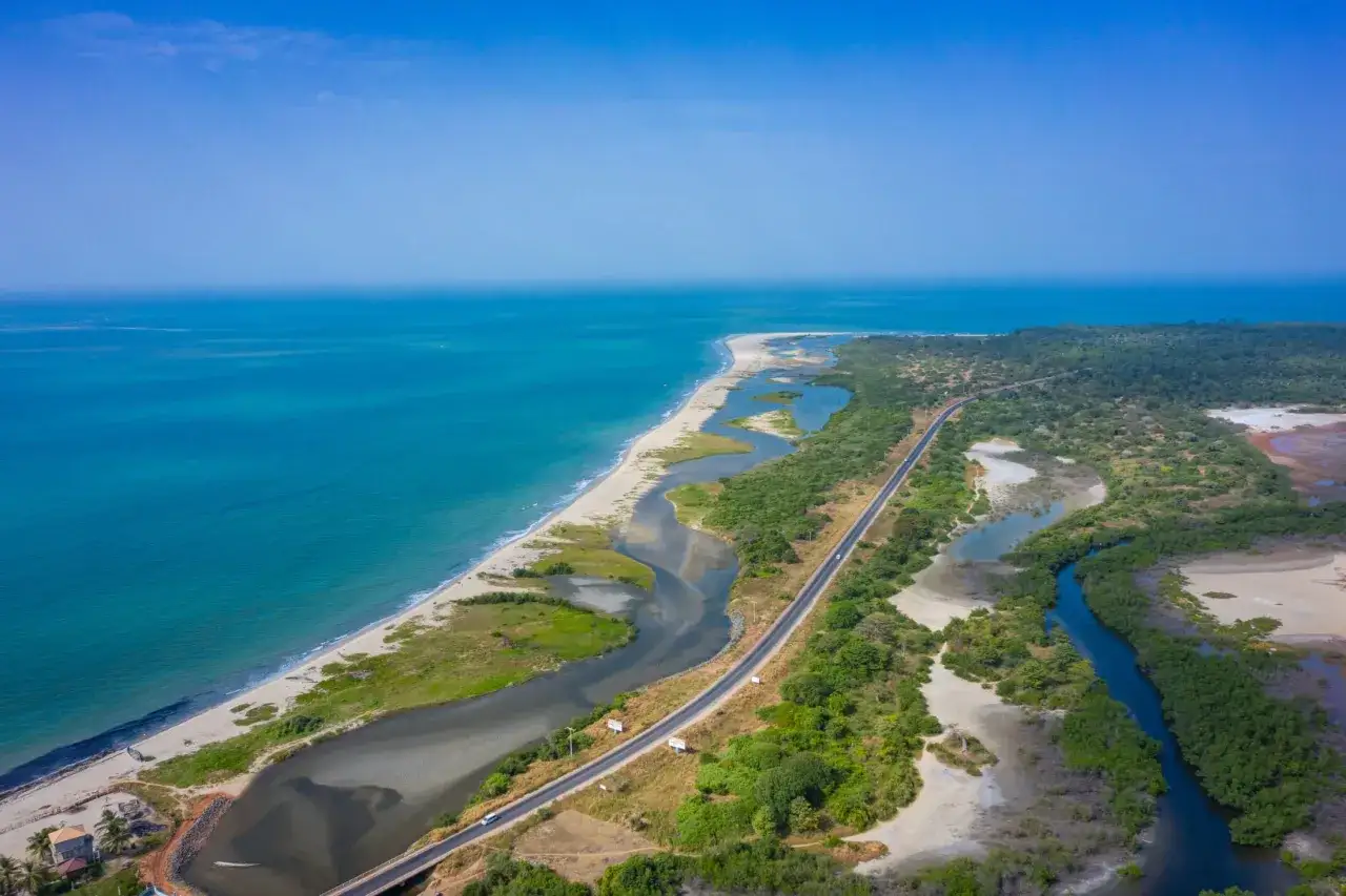 Malownicze gambia plaże z turkusowym oceanem, piaszczystym wybrzeżem i zielonymi namorzynami. Droga wije się wzdłuż wybrzeża.