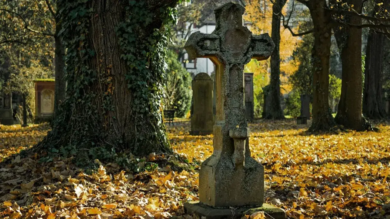 Kamienny krzyż na tle jesiennego cmentarza. Odkryj najpiękniejsze cmentarze zabytkowe w Polsce, które warto odwiedzić.