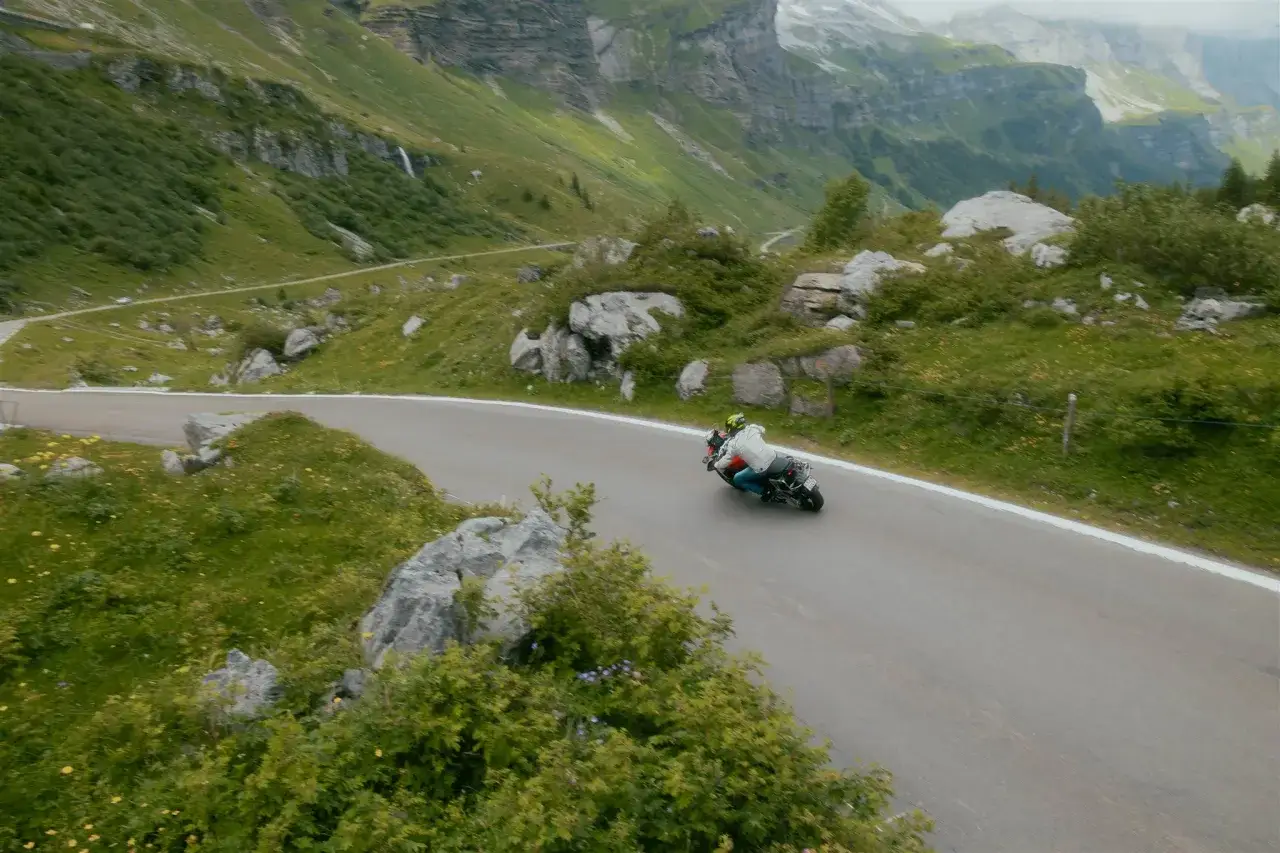 Motociclista affronta una curva in montagna, paesaggio alpino mozzafiato. Consigli per un viaggio in Svizzera in moto.
