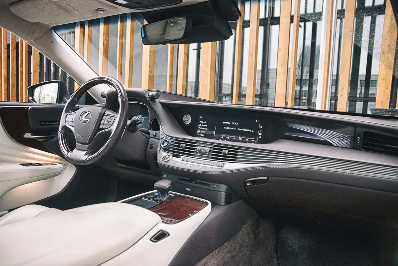 Wnętrze Lexus LS 500 z jasną tapicerką i drewnianymi wstawkami. Na ekranie multimediów widoczna stacja radiowa 