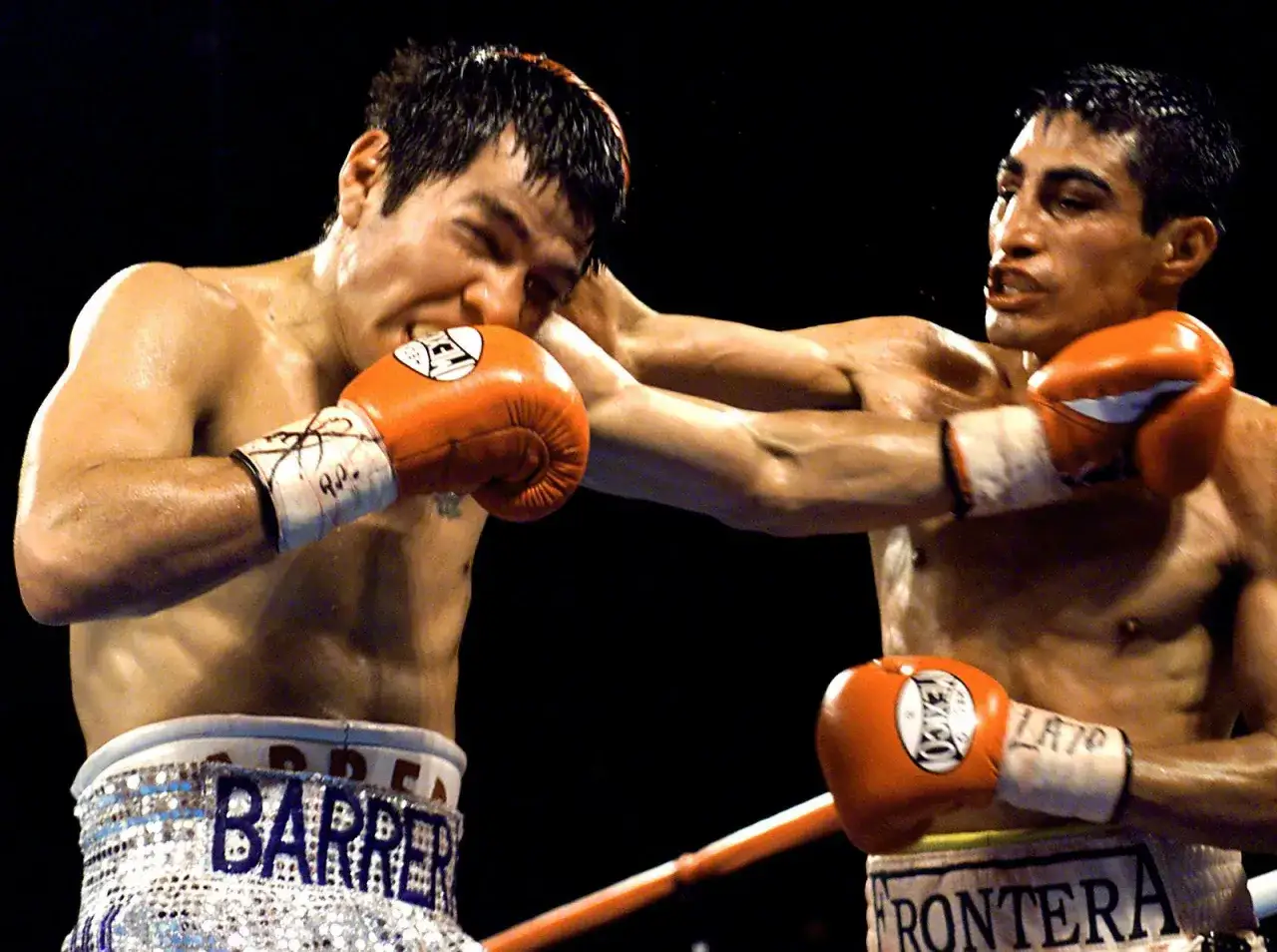 Two intense Mexican boxers exchange blows in the ring. One boxer lands a punch to the head of the other, who winces in pain.