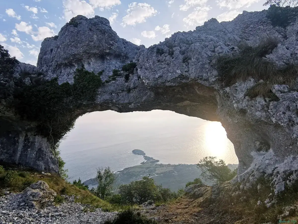 Un arco de roca natural, el ojo del diablo, enmarca una vista del mar y el sol poniente.