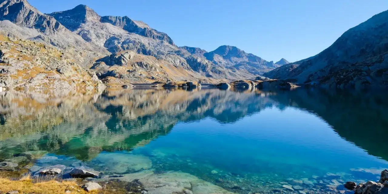 Lac d'altitude aux eaux turquoise, refl&eacute;tant les montagnes rocheuses du massif de Belledonne. Une carte naturelle de s&eacute;r&eacute;nit&eacute;.