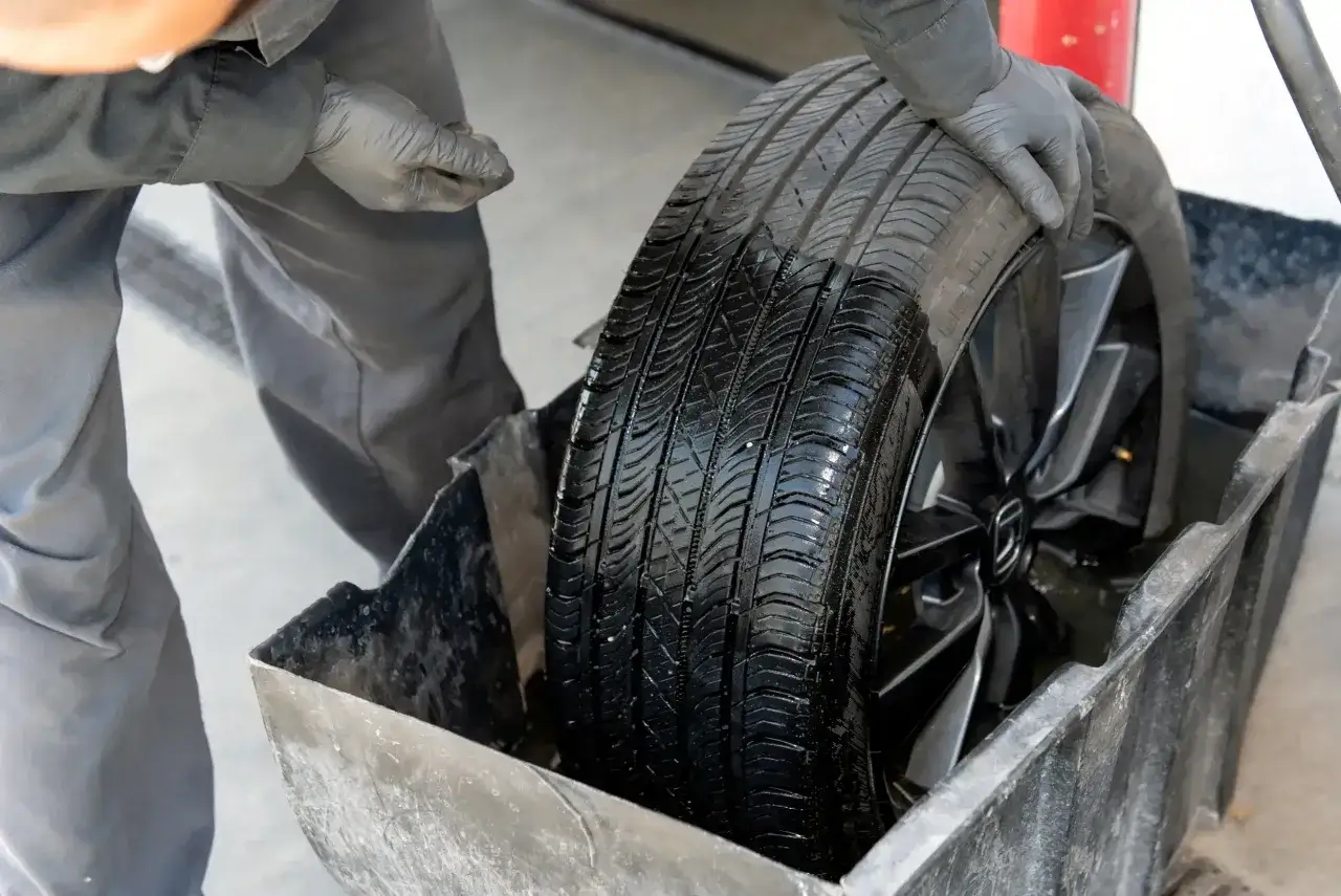 Mecánico revisa un neumático de coche mojado en un recipiente, buscando si hay algún pinchazo.
