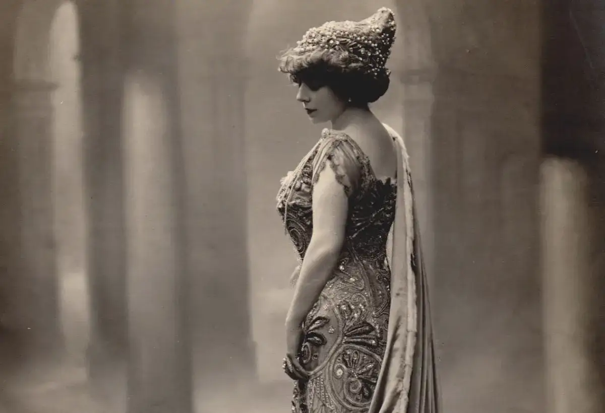 Eleganza d'altri tempi in un ritratto di fotografi di moda. Una donna con un elaborato copricapo e un abito riccamente decorato posa con grazia.