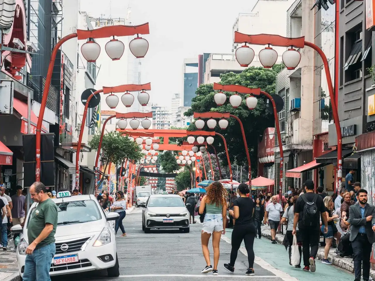 Bunte Lampions schmücken die Straße in São Paulo. Menschen flanieren, Autos fahren, ein lebendiges Stadtbild.