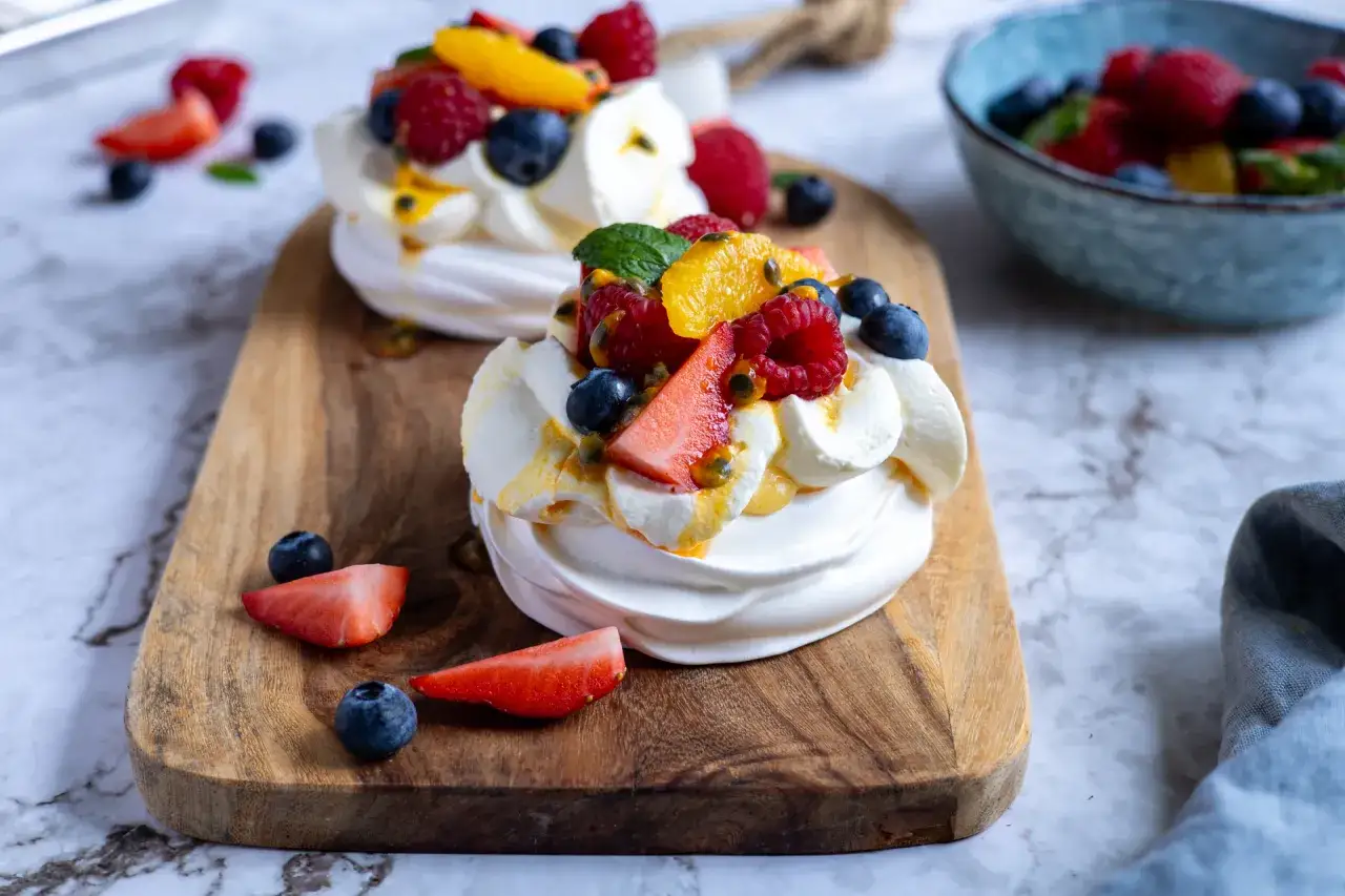Tv&aring; l&auml;ckra pavlova bakelser med gr&auml;dde och f&auml;rska b&auml;r som jordgubbar, bl&aring;b&auml;r och hallon.
