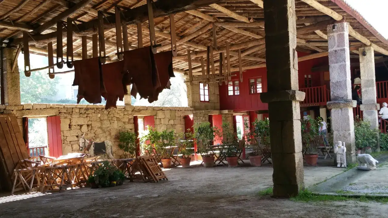 Un lugar r&uacute;stico con cueros colgados, perfecto para comer en Allariz. Mesas, sillas y un burro decoran el patio.