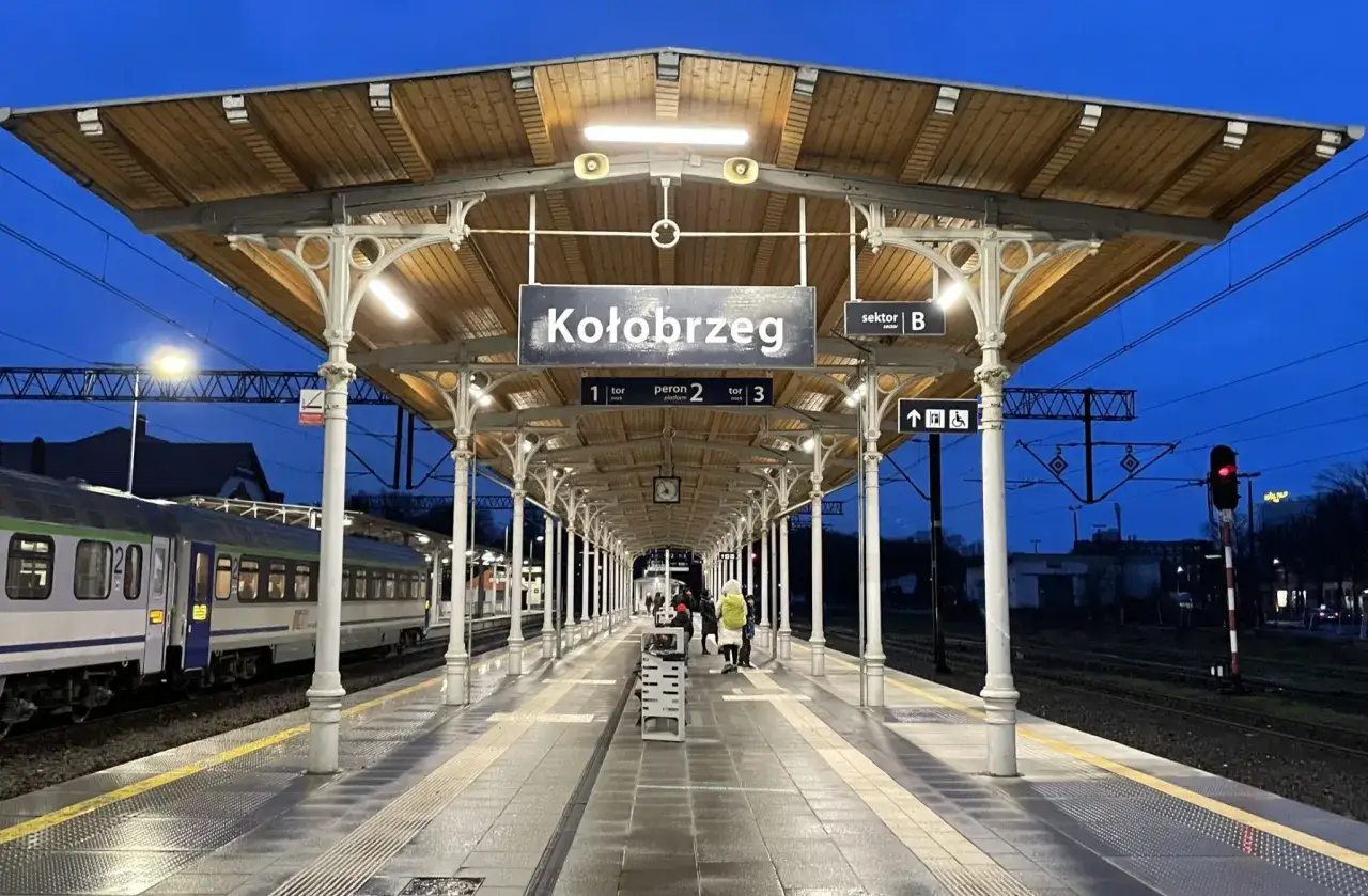 Dworzec w Kołobrzegu, wieczór. Pociąg na torze 1. Znak informuje, jak dojechać do Kołobrzegu.