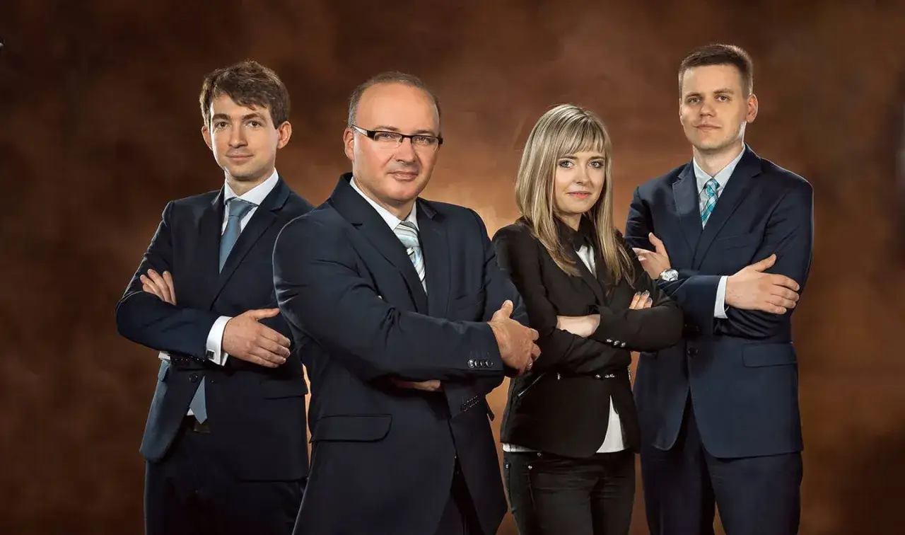 Cztery osoby w garniturach stoją ze skrzyżowanymi ramionami na brązowym tle.