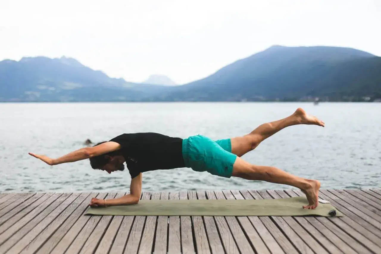 Un homme en planche latérale, bras tendu, jambe levée, sollicitant ses abdos bas du ventre face à un lac et des montagnes.