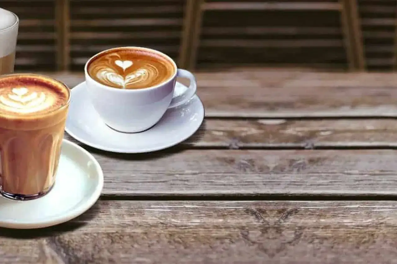 Due tazze di caffè con schiuma artistica, una in vetro e una in ceramica, mostrano la differenza tra cappuccino e caffè latte.
