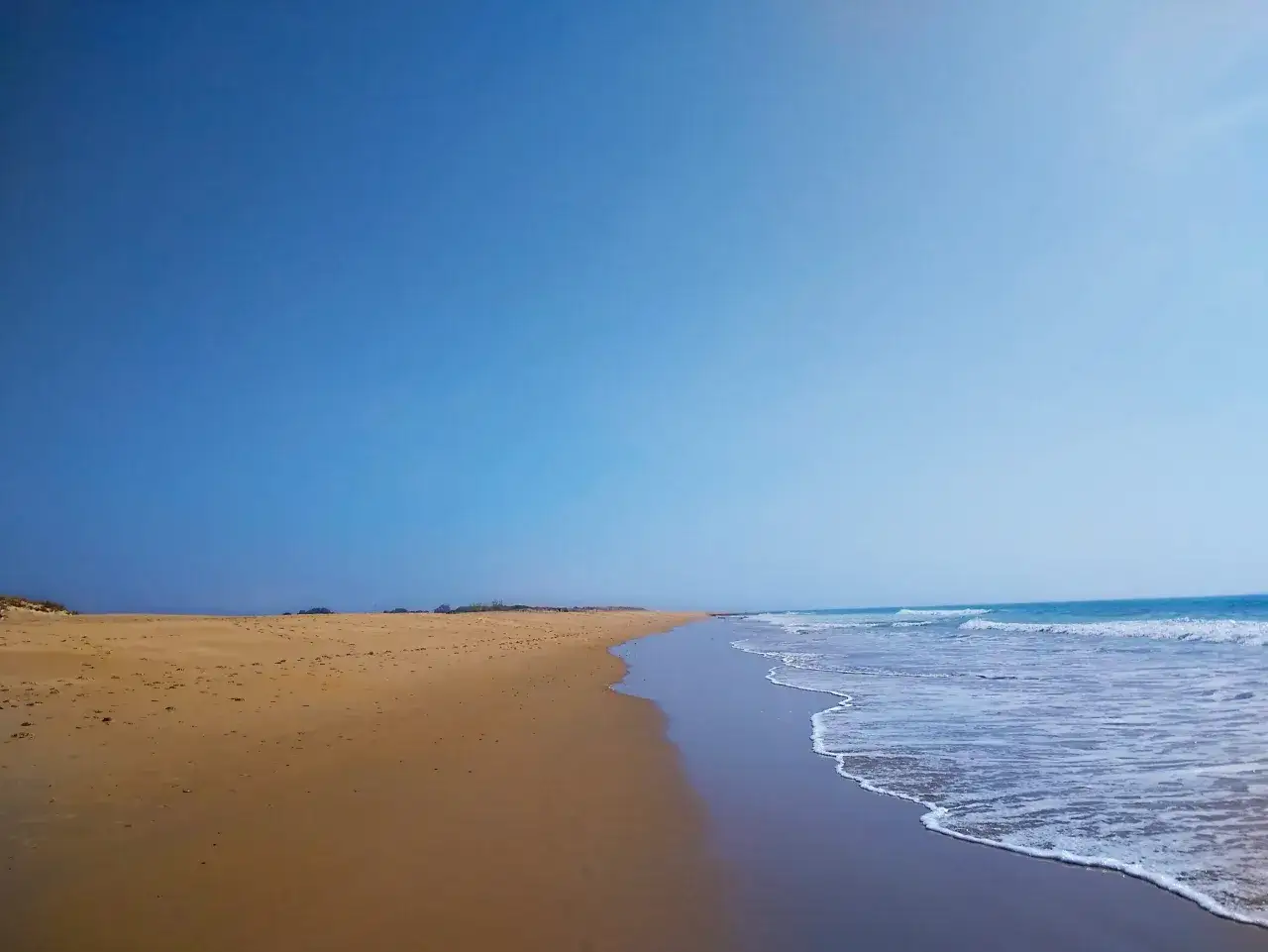 Pusta plaża z piaskiem i falami, idealne miejsce na spacer po molo w Łebie.
