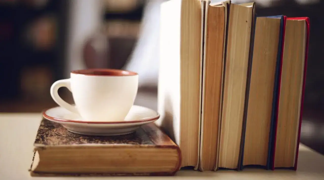 Kubek kawy na starym tomie, obok stosu książek o kawie. Idealne popołudnie dla miłośnika literatury i aromatycznego napoju.
