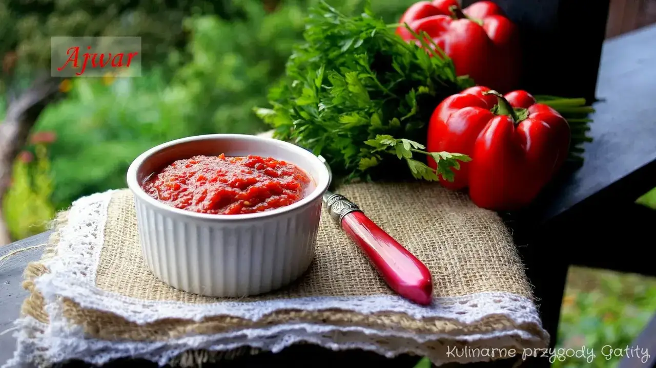 Ajvar, czyli pasta z pieczonej papryki i bakłażana, w miseczce. Obok świeża natka i czerwone papryki.