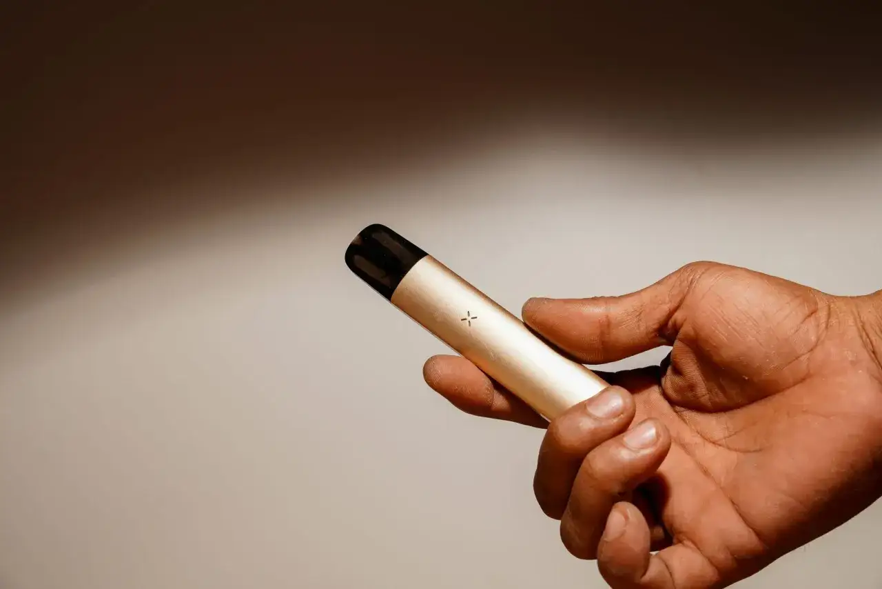 Mano sosteniendo un vaporizador dorado, similar a un diseño de Herbert A. Gilbert.