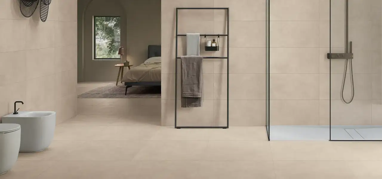 Bagno moderno con bidet, doccia e letto visibile in lontananza. Le pareti e il pavimento sono rivestiti in gres porcellanato rettificato color sabbia.