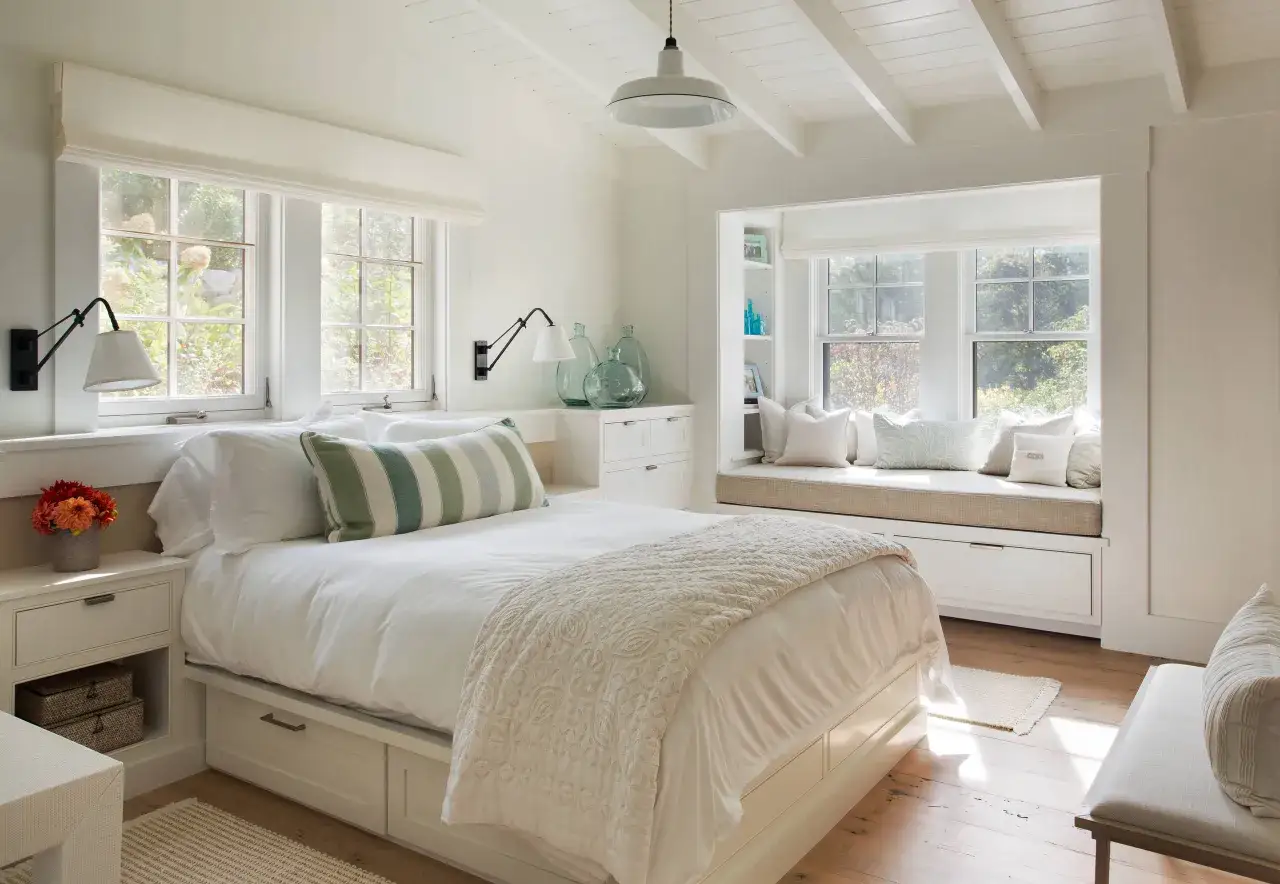 Habitaci&oacute;n luminosa con cama blanca, almohadas a rayas y un banco junto a la ventana. A pesar de ser habitaciones muy peque&ntilde;as, el dise&ntilde;o maximiza el espacio.