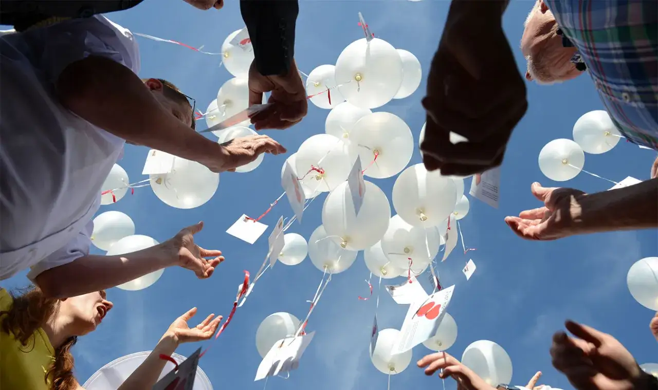 H&auml;nde lassen wei&szlig;e Luftballons zur Hochzeit steigen. Kleine Karten mit W&uuml;nschen schweben mit ihnen in den blauen Himmel.