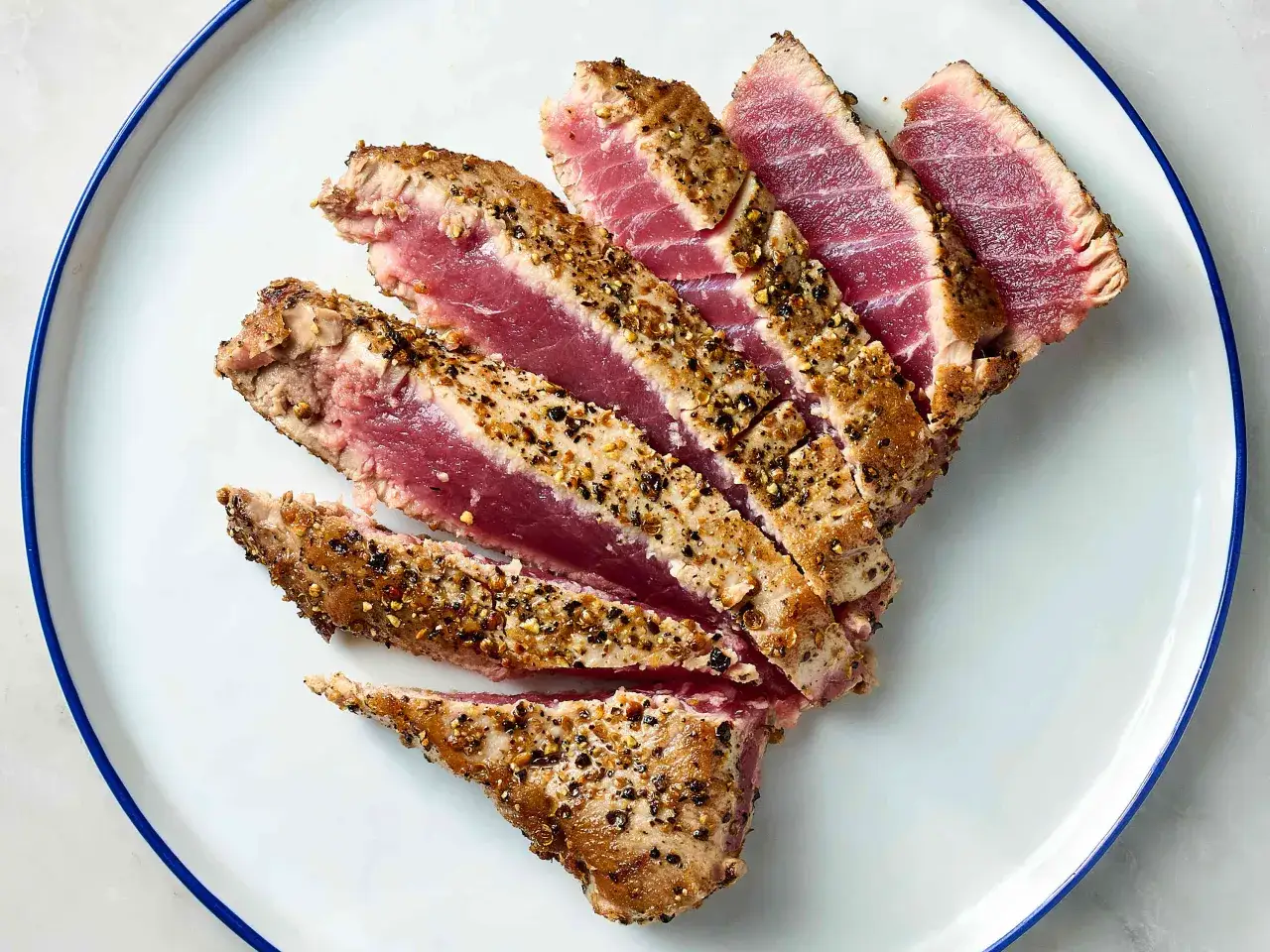 Rodajas de atún a la plancha, con un exterior dorado y un interior rosado, cubiertas de especias y pimienta negra.