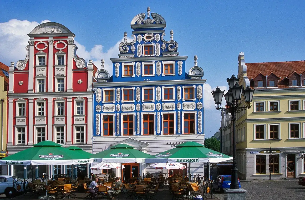 Kolorowe kamienice na **rynku Szczecin** z ogródkiem kawiarnianym pod zielonymi parasolami.