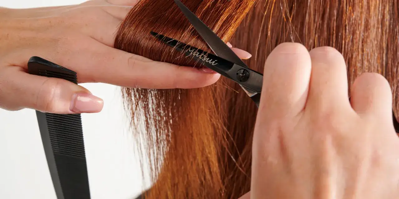Precyzyjne cięcie nożyczkami podczas hair dusting rudych włos&oacute;w. Grzebień czeka na swoją kolej.
