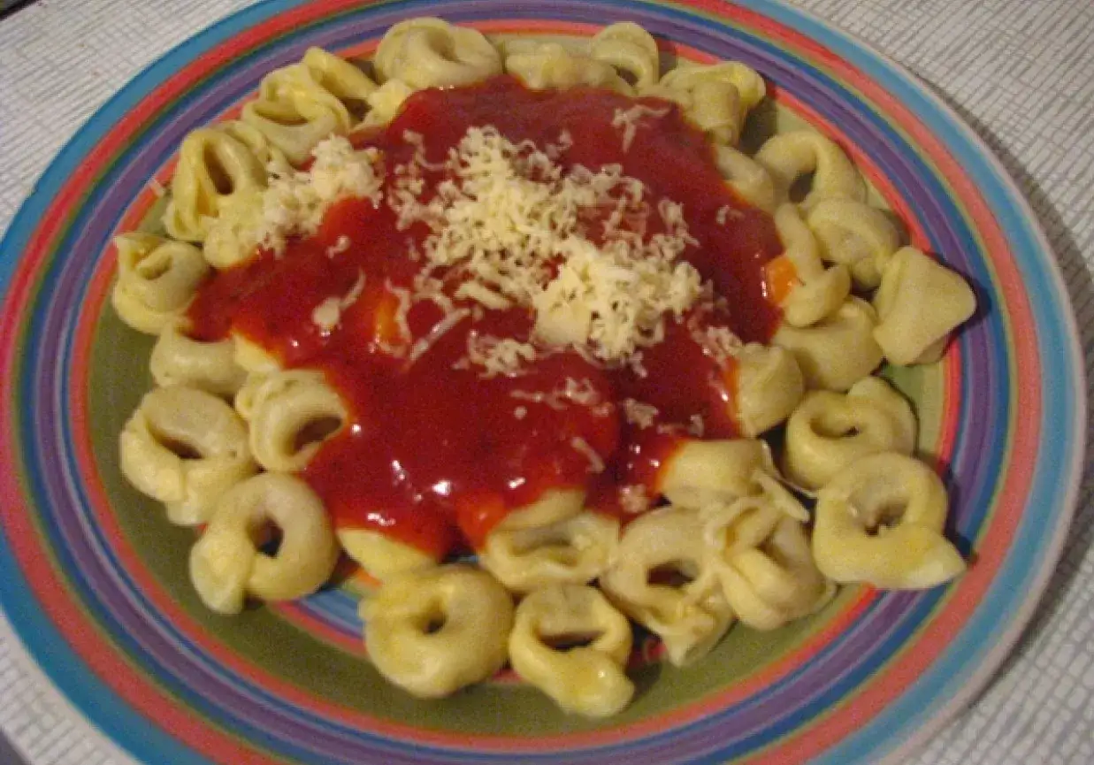 Tortellini z bogatym sosem pomidorowym i startym serem na kolorowym talerzu. Pyszny sos do tortellini czeka!