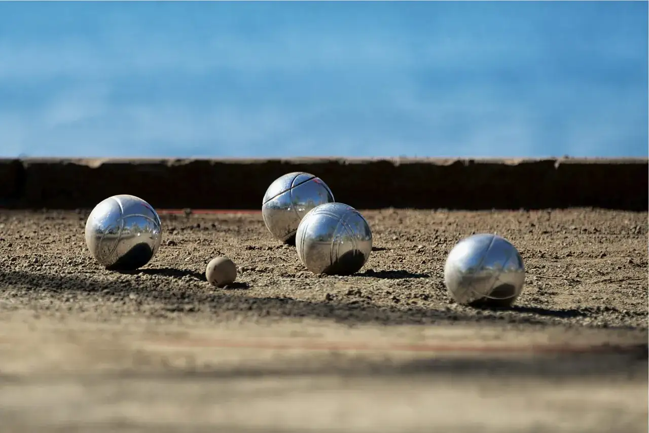 Sur un terrain de p&eacute;tanque, diff&eacute;rents jeux de boules brillent sous le soleil, pr&ecirc;ts pour une partie anim&eacute;e.