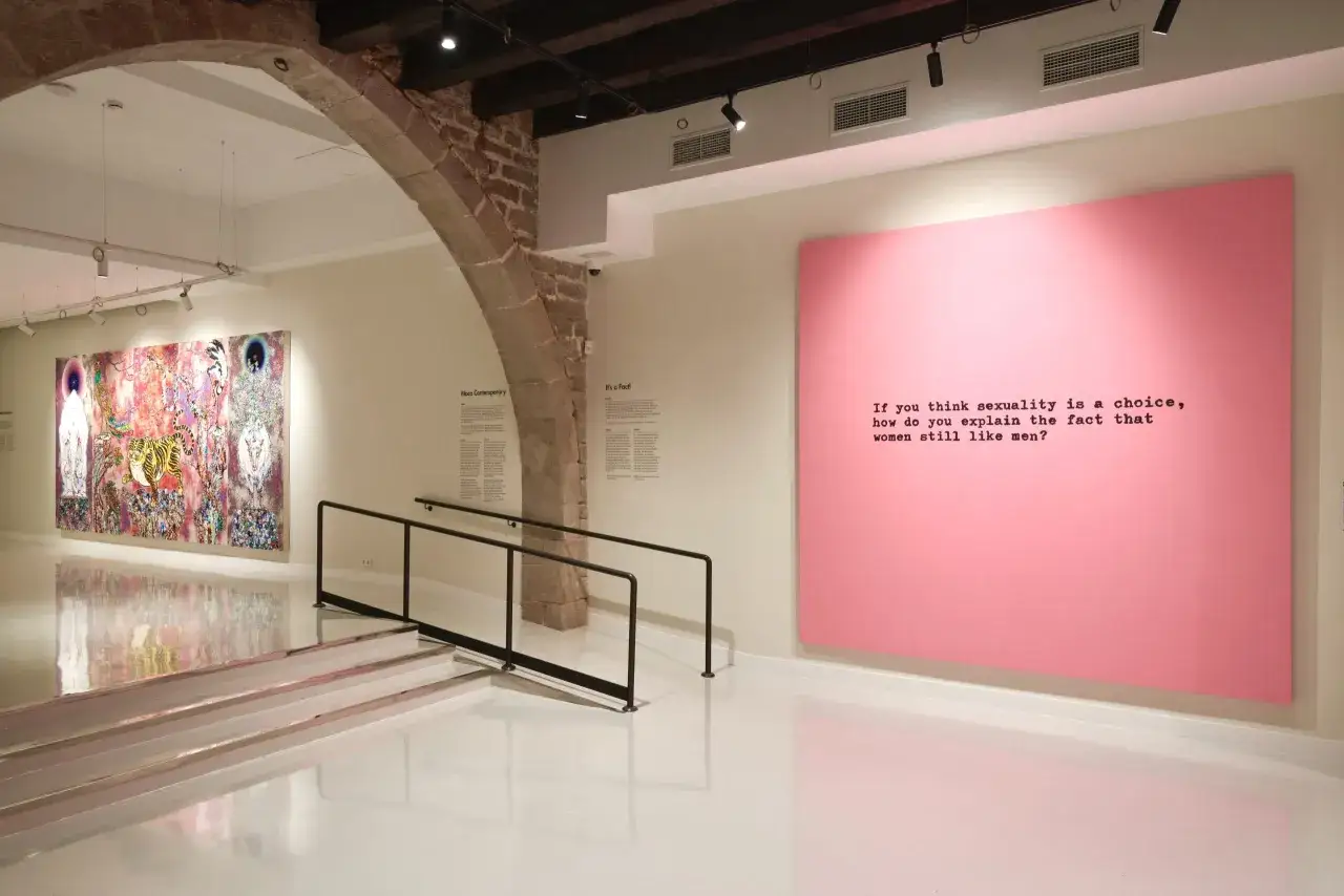 Eine Ausstellung mit farbenfrohen Kunstwerken und einem provokanten Zitat von Hayden Kays auf einer rosa Leinwand.