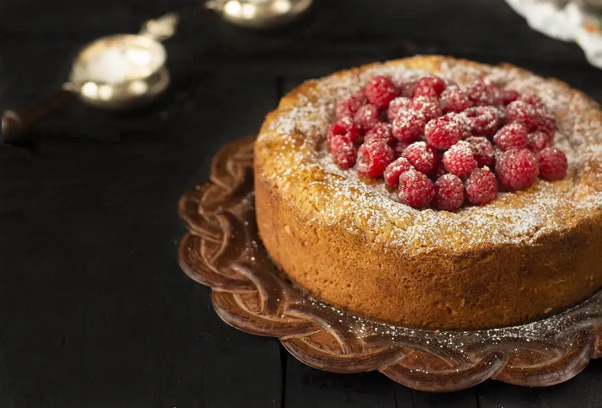 Delicioso pastel vasco cubierto de frambuesas frescas y azúcar glas, servido en un plato decorativo.