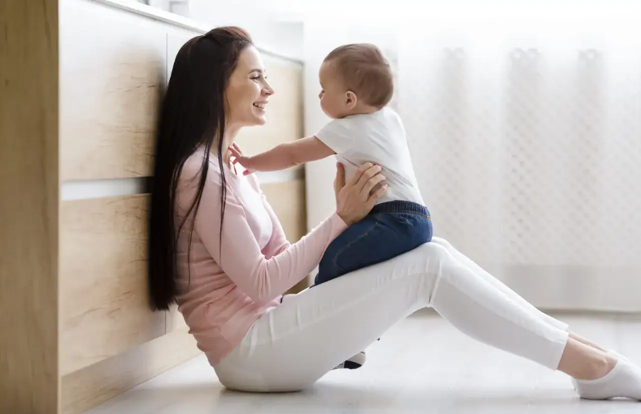 Uśmiechnięta kobieta z dzieckiem na kolanach. Zastanawiasz się, ile zarabia niania miesięcznie?