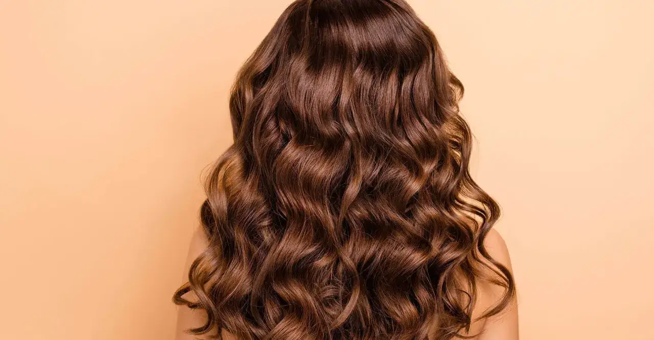 Cabello casta&ntilde;o oscuro, largo y con ondas naturales, un pelo colocho que cae en cascada sobre un fondo liso color melocot&oacute;n.