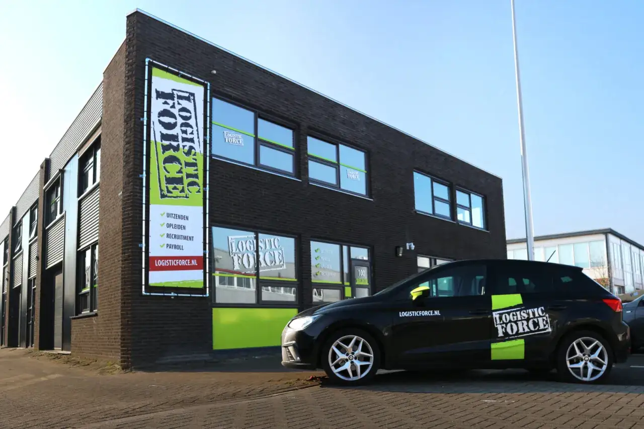 Kijk voor logistic force **oferty pracy** op de banner bij het gebouw. Een zwarte auto met logo staat geparkeerd.