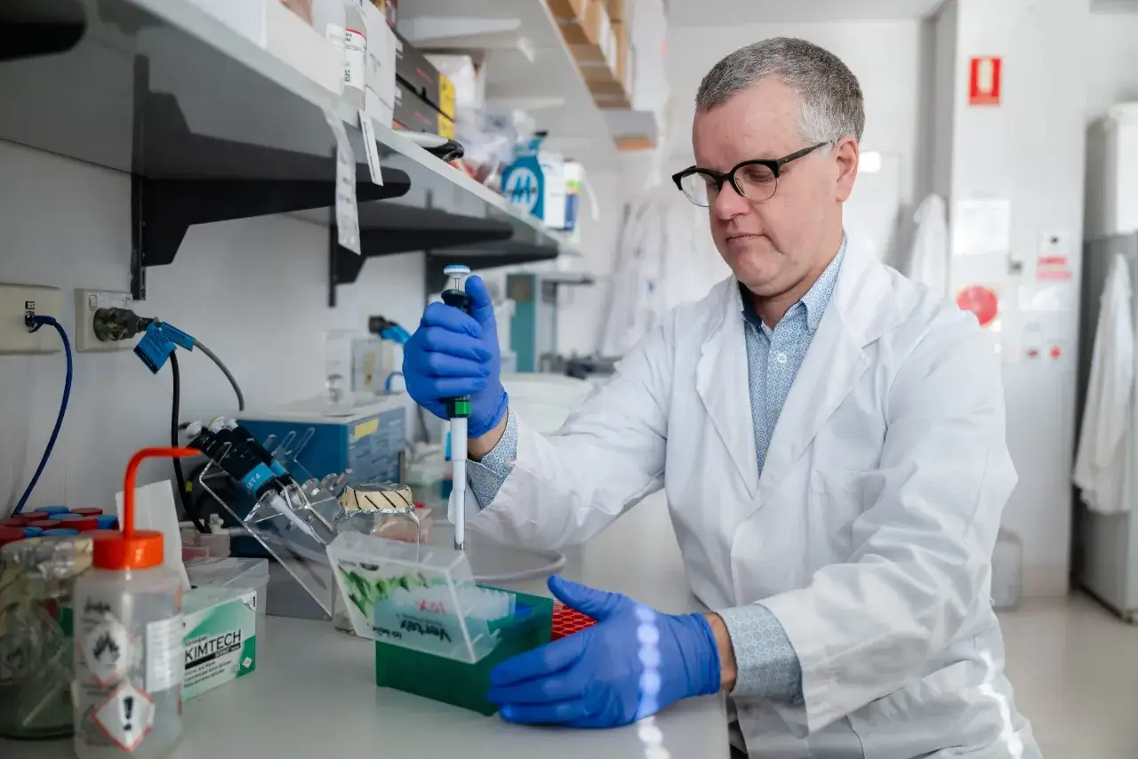 Naukowiec w białym fartuchu i niebieskich rękawiczkach wykonuje precyzyjne czynności laboratoryjne, przygotowując próbki do testu na cukrzycę.