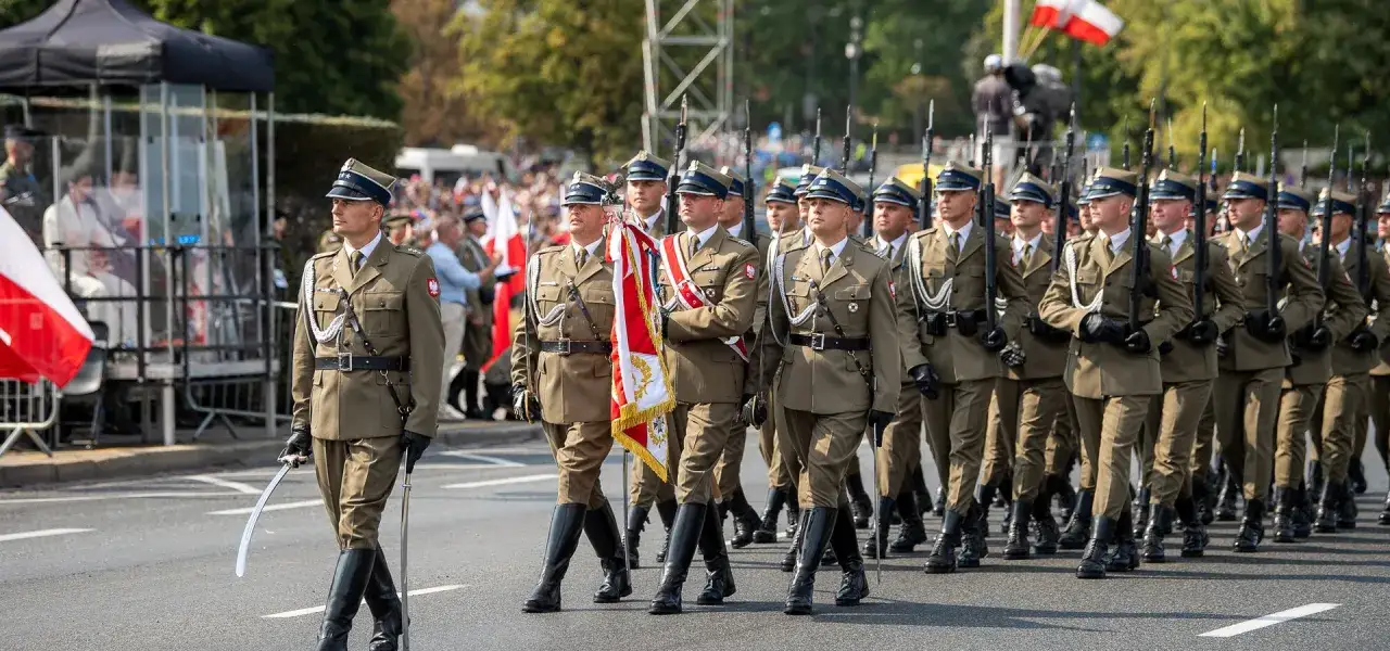 Żołnierze maszerują w defiladzie z biało-czerwoną flagą. Obchody Święta Wojska Polskiego 15 sierpnia.