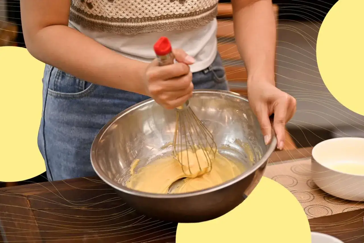 Hände schlagen weiche Butter mit einem Schneebesen in einer Schüssel zu einer cremigen Masse.