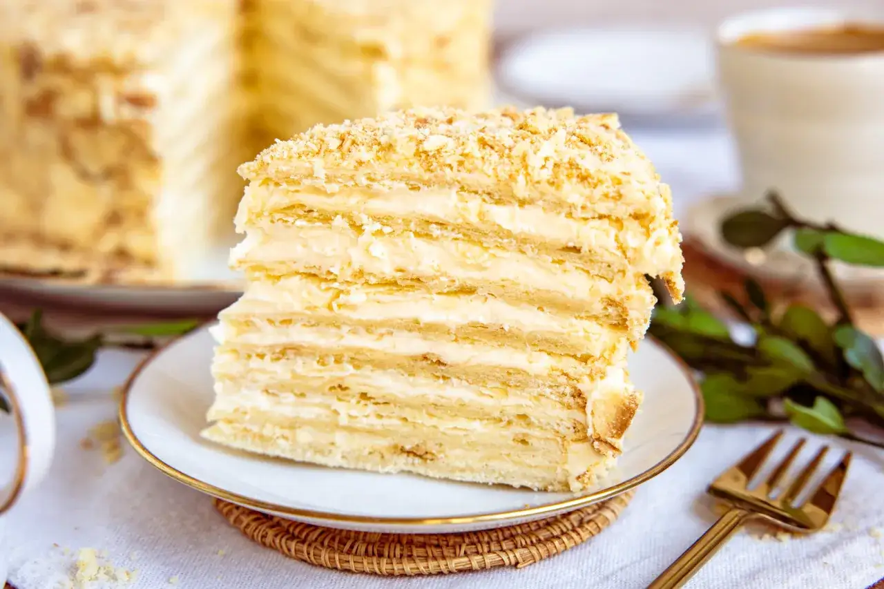 Ein Stück Napoleon Torte mit vielen Schichten Blätterteig und cremiger Füllung, bestreut mit Krümeln.