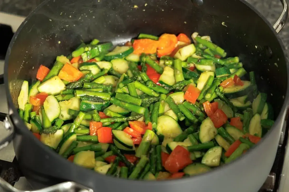 Verduras salteadas en una sartén: espárragos, calabacín y pimientos rojos, listas para mezclar con pasta.