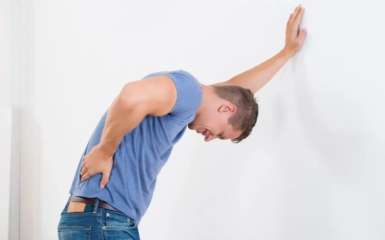 Uomo con mal di schiena da freddo appoggiato al muro, cerca rimedi.
