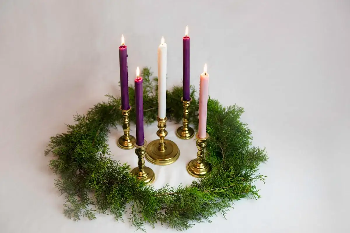 Five lit candles, three purple, one white, and one pink, stand in brass holders on a green evergreen wreath. These are the 4th Sunday of Advent readings.