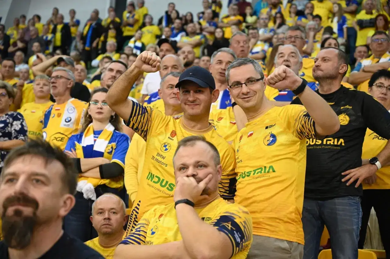 Fani w ż&oacute;łtych koszulkach z logo Aalborg Handball kibicują swojej drużynie.
