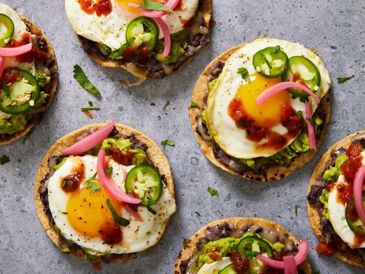 Pyszne śniadanie bez glutenu: tostadas z jajkiem sadzonym, awokado, fasolą i piklowaną cebulką.