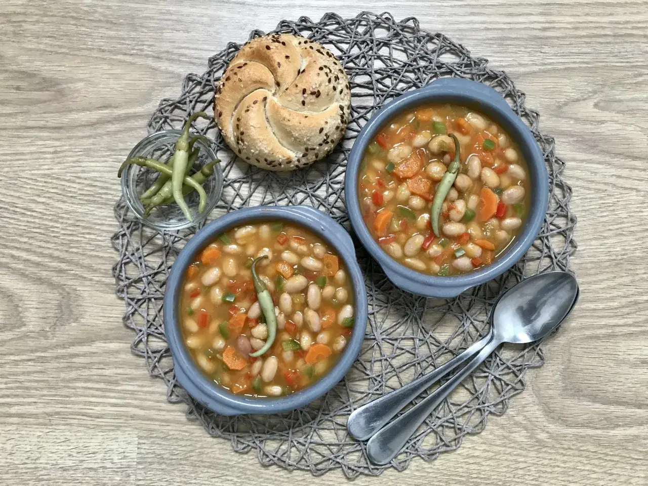 Dos cuencos de pochas a la navarra, con un panecillo y pimientos guindilla.