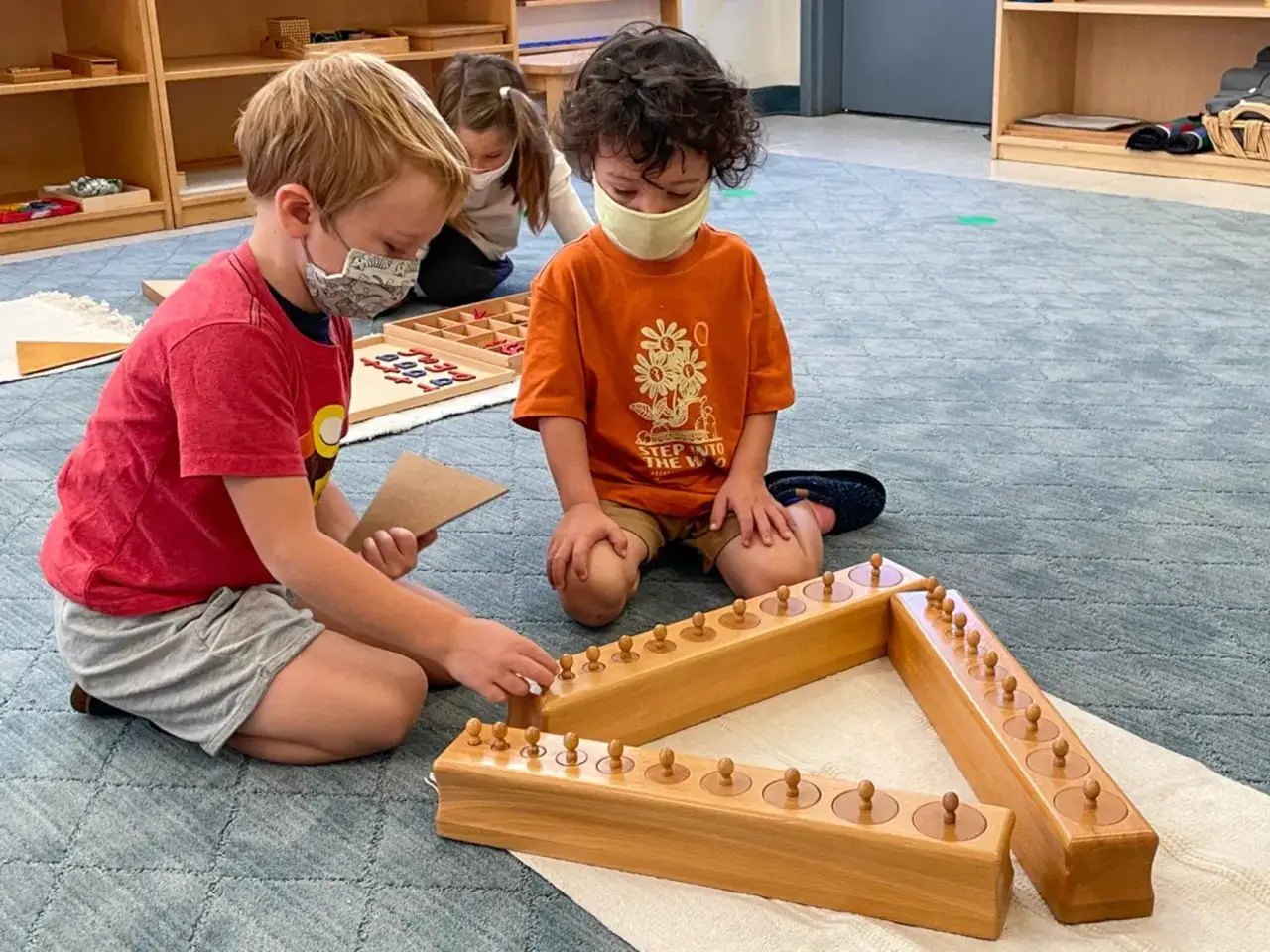 Bambini con mascherine giocano con cilindri Montessori, un esempio di giochi montessori 2 anni fai da te.
