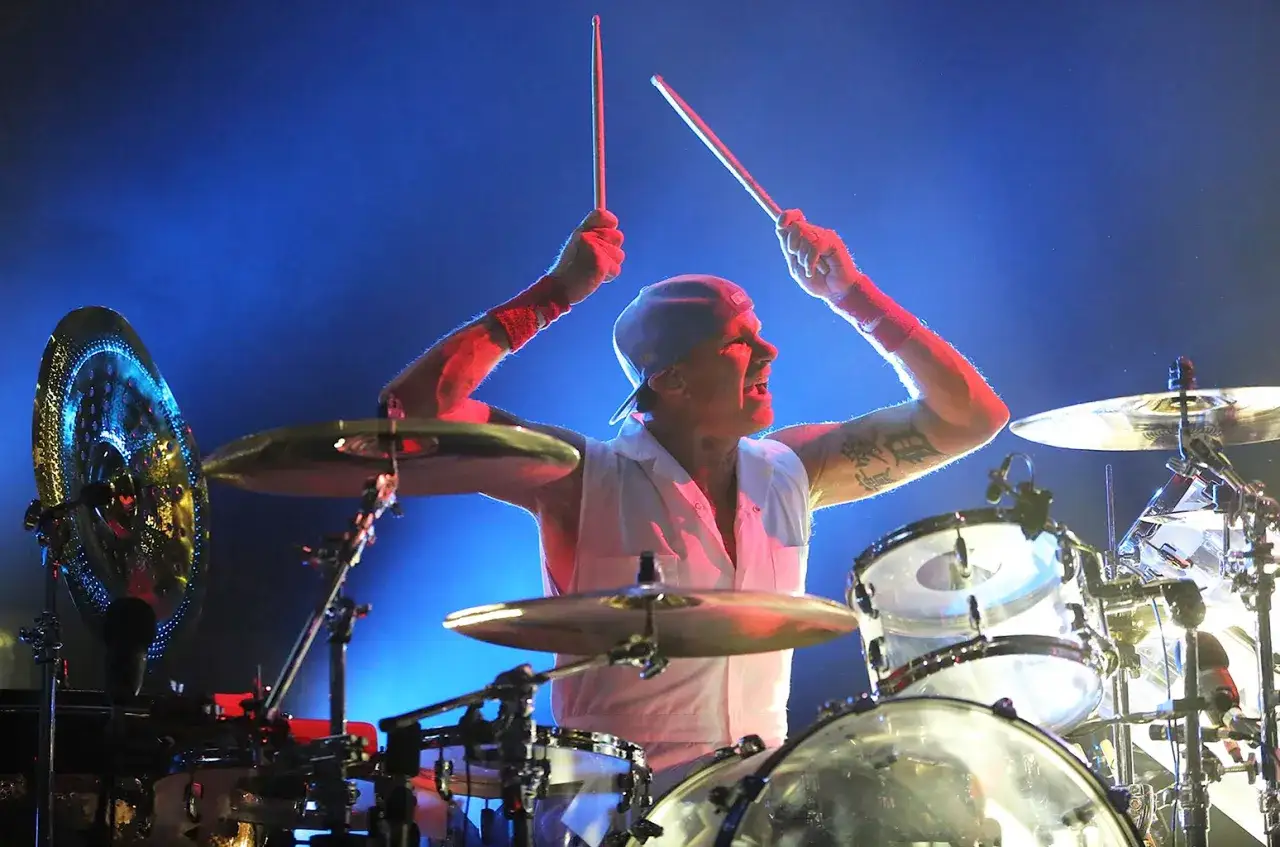 Chad Smith, the powerhouse drummer for his band, is captured mid-performance, sticks raised, driving the rhythm with intense focus.