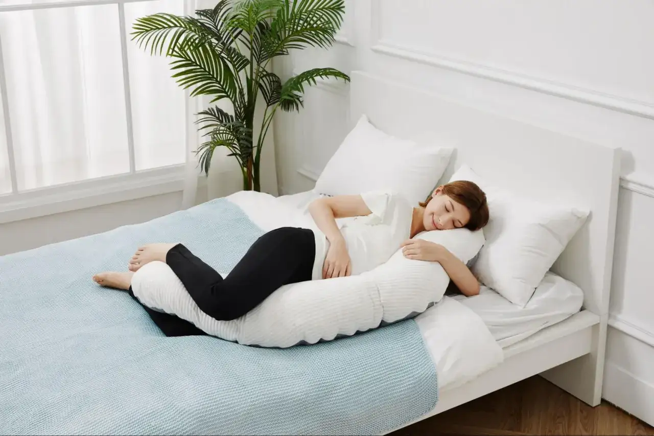 Mujer embarazada durmiendo de lado, abrazando una almohada de cuerpo completo. Las posturas de dormir en el embarazo son clave para el descanso.